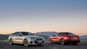 A white and red 2024 BMW 5 Series gas and electric sedan parked next to each other