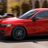 A side profile shot of a 2024 Honda Civic Hatchback model in Rallye Red driving through a city