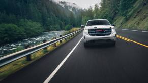 A 2024 GMC Sierra pickup truck driving on a tree-covered mountainous road