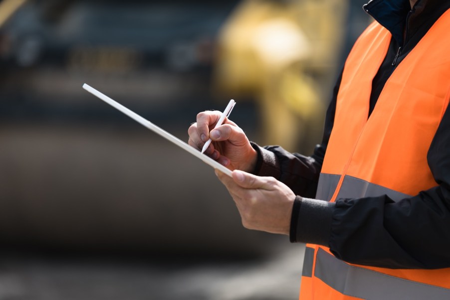 Man in orange neon vest holds a clipboard at a car auction.